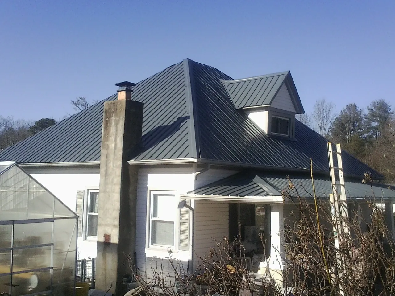 Dark blue standing seam metal roof on a white farmhouse with dormer — Slate & Tile Roof Repair by Roofing Brothers in Wever