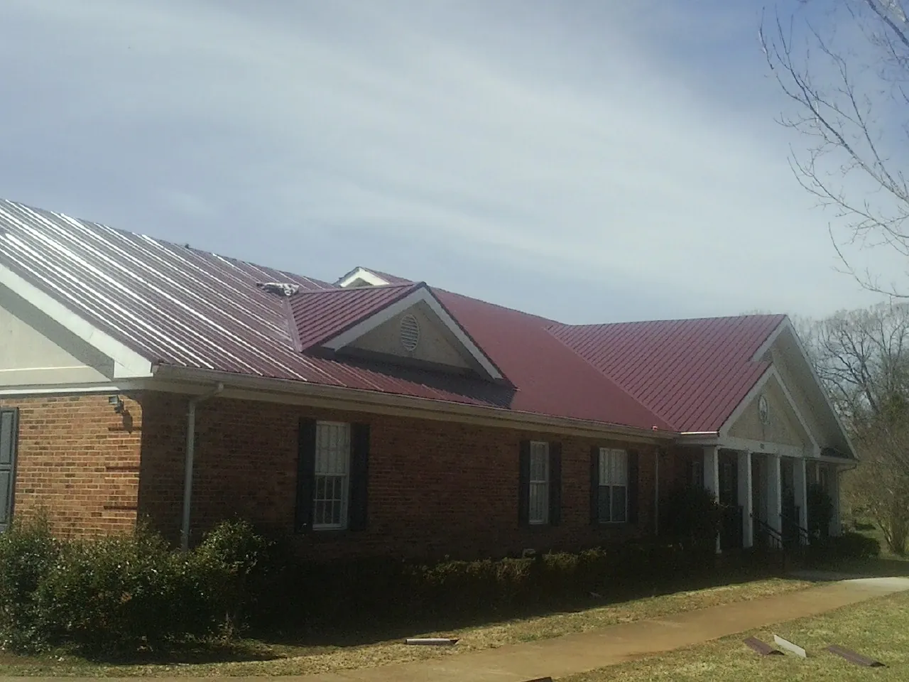 Red metal roof with gabled entries on a long brick building, from a Hail Damage Roof Repair job in Wever