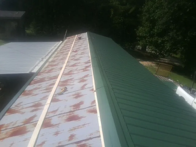 Old rusted panels beside newly installed green metal roofing — Wind Damage Roof Repair by Roofing Brothers in Wever