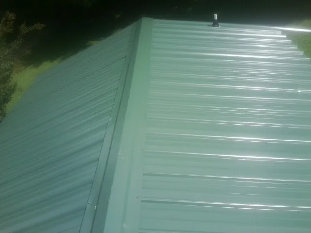 New green metal panels meeting at the ridge of a roof — Flat Roof Repair work by our crew in Wever