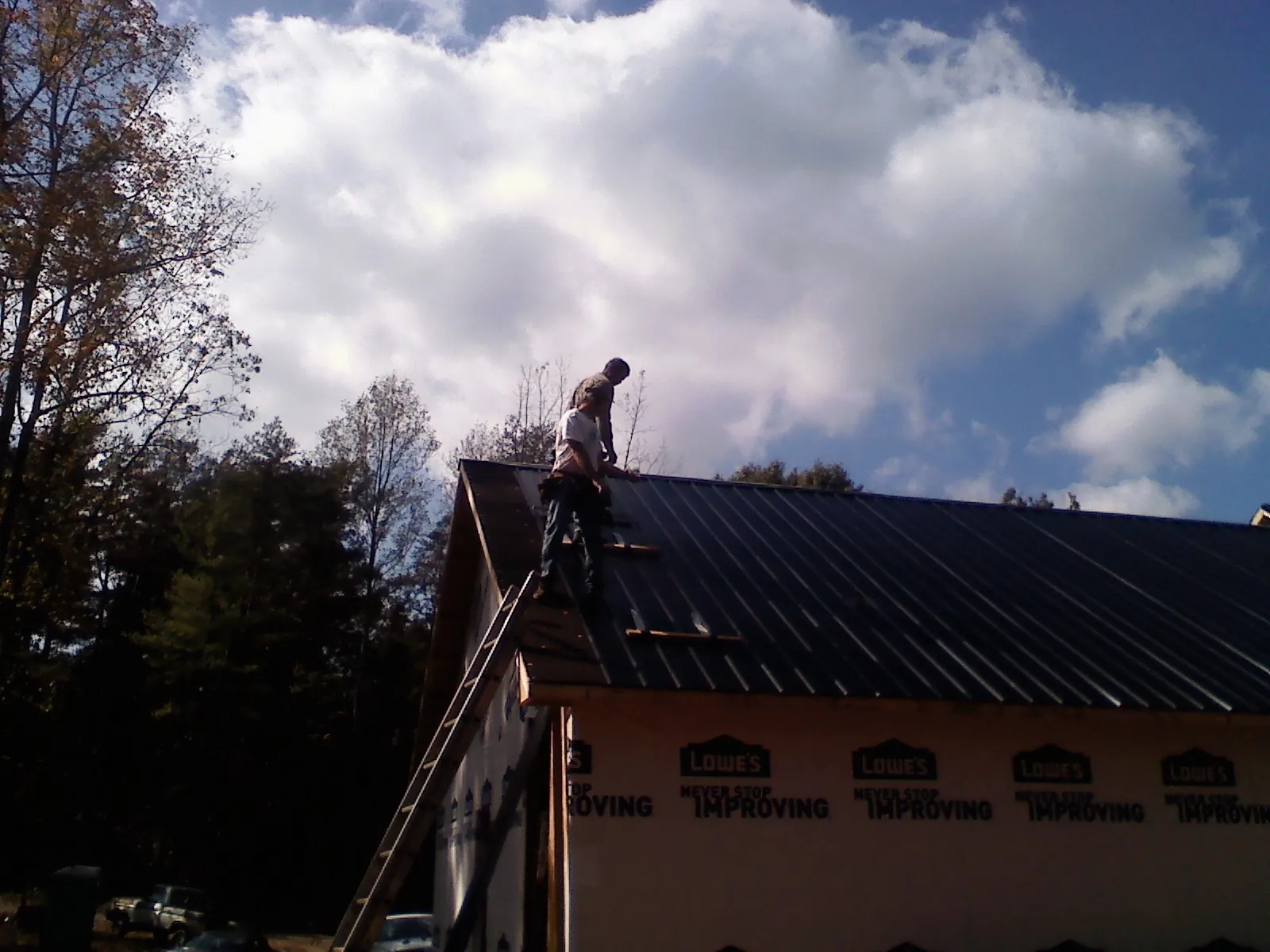 Roofer fastening dark metal panels high against a cloudy sky, from a Roof Inspection job in Wever