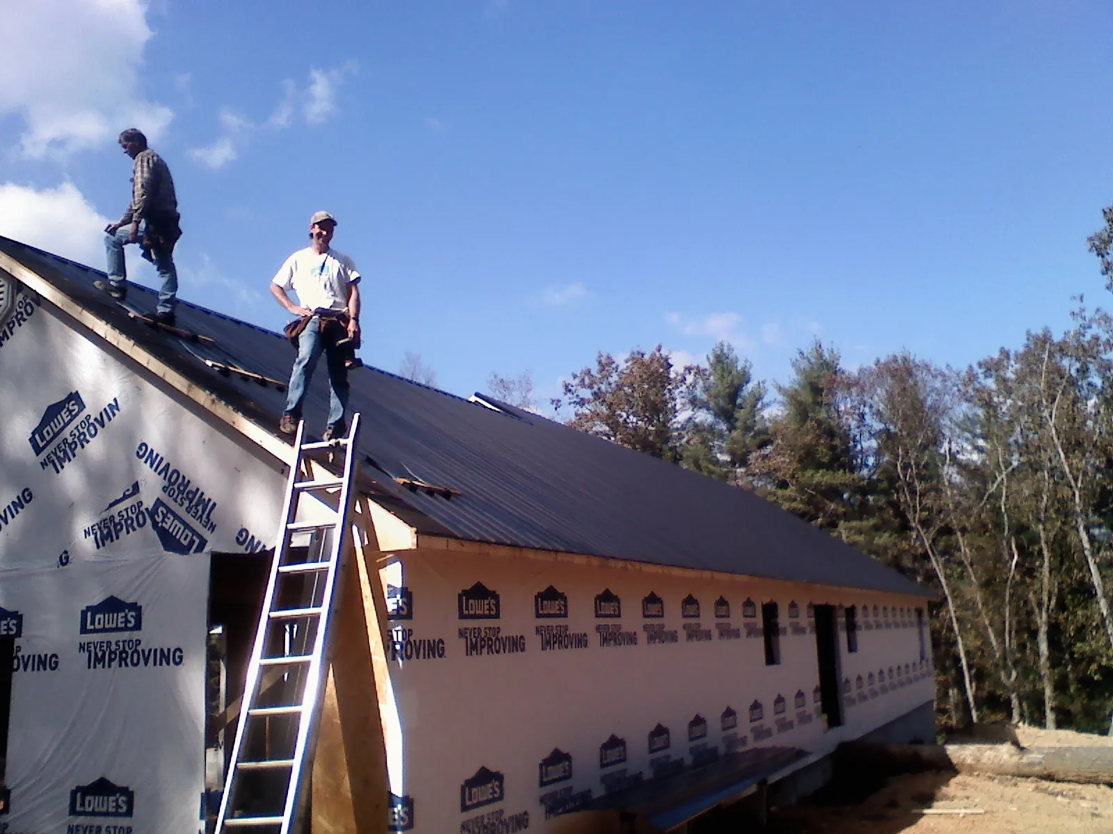 Two roofers standing on a long dark metal roof over a wrapped building in Wever