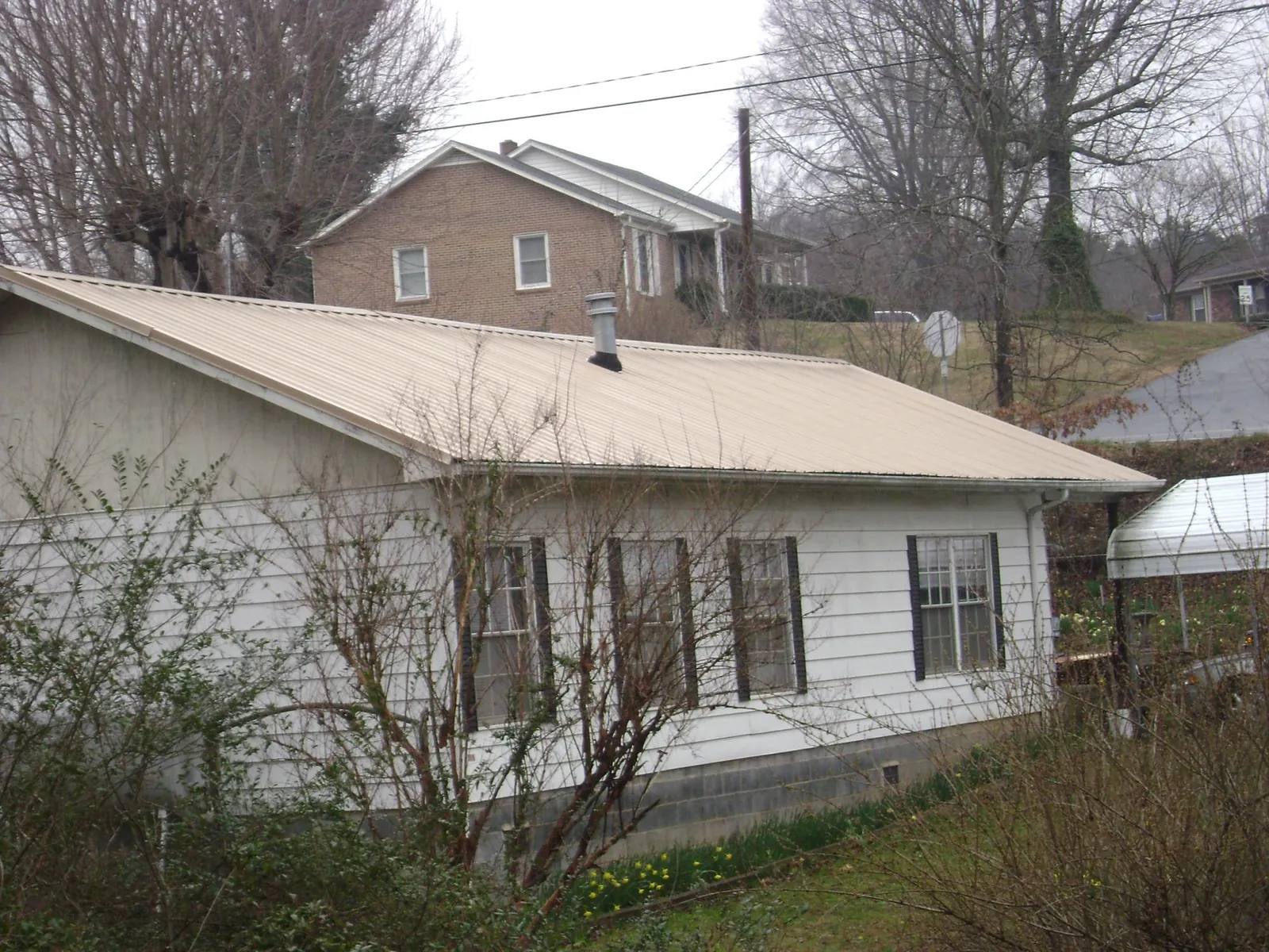 Tan metal roof on a white sided house set into a hillside — Commercial Roofing by Roofing Brothers in Wever