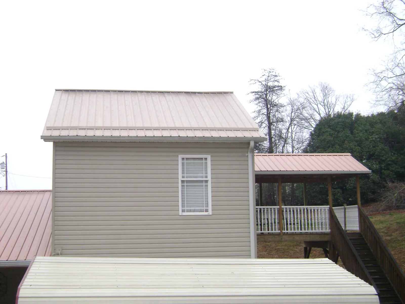 Tan metal roofs on a two story addition and attached porch, from a Roof Replacement job in Wever