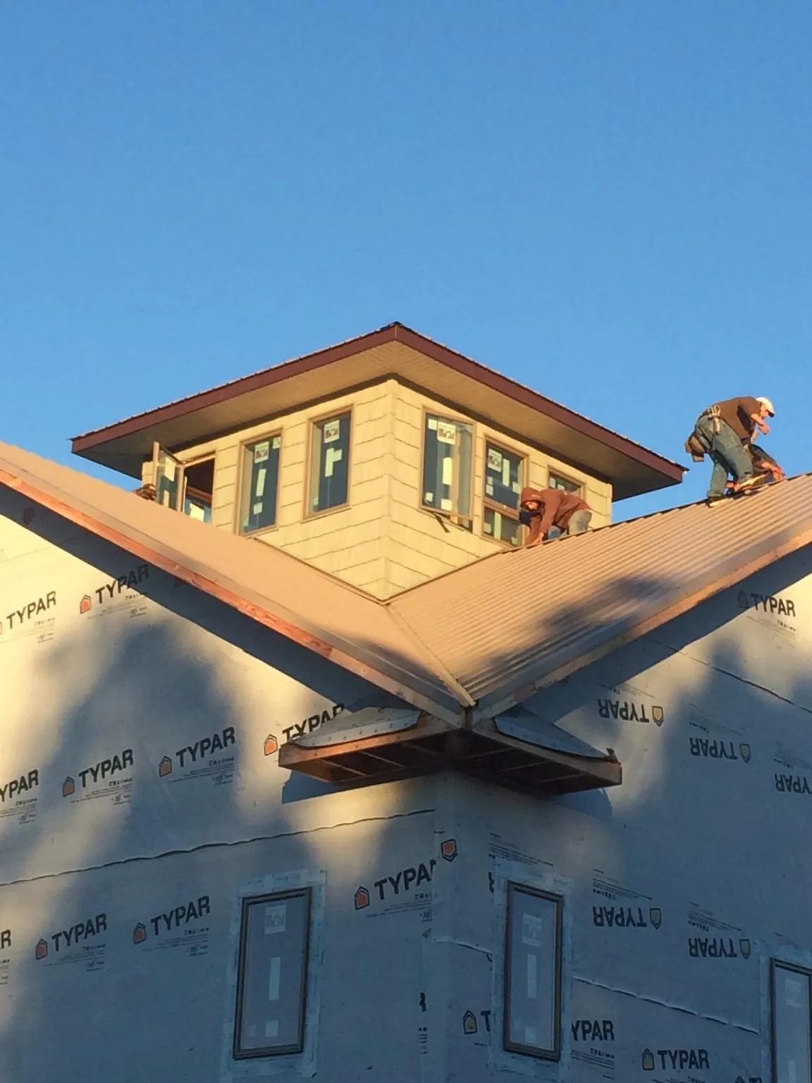 Roofers working around a rooftop cupola on a new metal roof at sunset — Roof Waterproofing in Wever by Roofing Brothers
